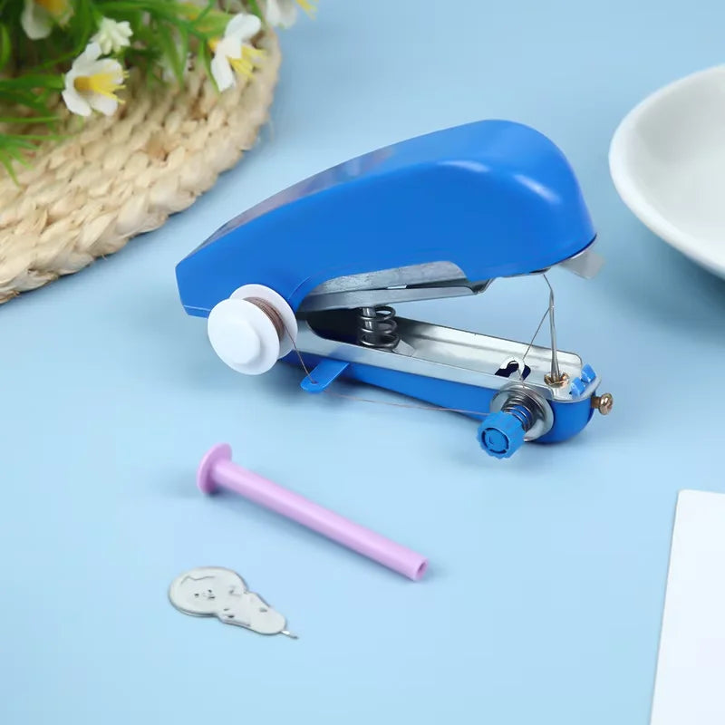 A blue portable handheld sewing machine is shown on a light blue surface next to a pink pin and a small metal piece.