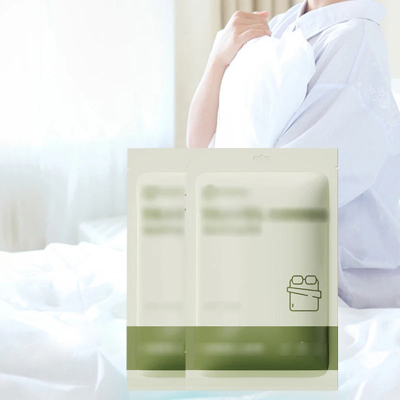 Une personne tient un emballage de draps de lit jetables avec une étiquette vert clair sur fond blanc.