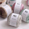 Three skeins of MuYuan glitter yarn in various shades are displayed on a white surface.