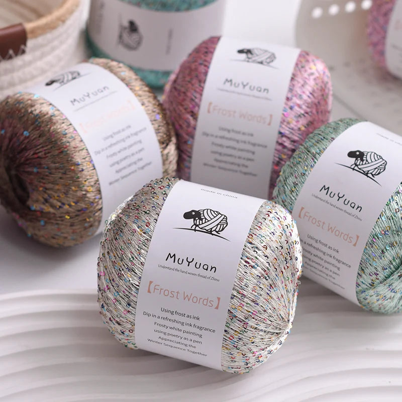 Three skeins of MuYuan glitter yarn in various shades are displayed on a white surface.