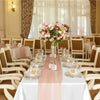 A white table set with a pink satin runner and floral centerpiece in a bright, elegant dining room.