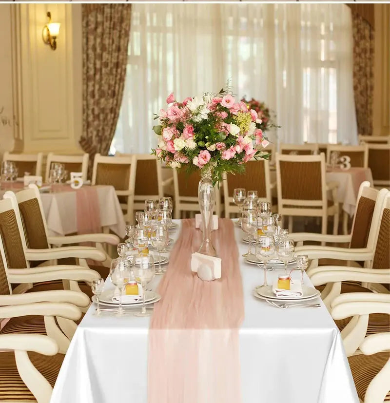 A white table set with a pink satin runner and floral centerpiece in a bright, elegant dining room.