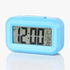 A light blue compact LED digital alarm clock displaying 12:00, with a display showing the date and temperature.
