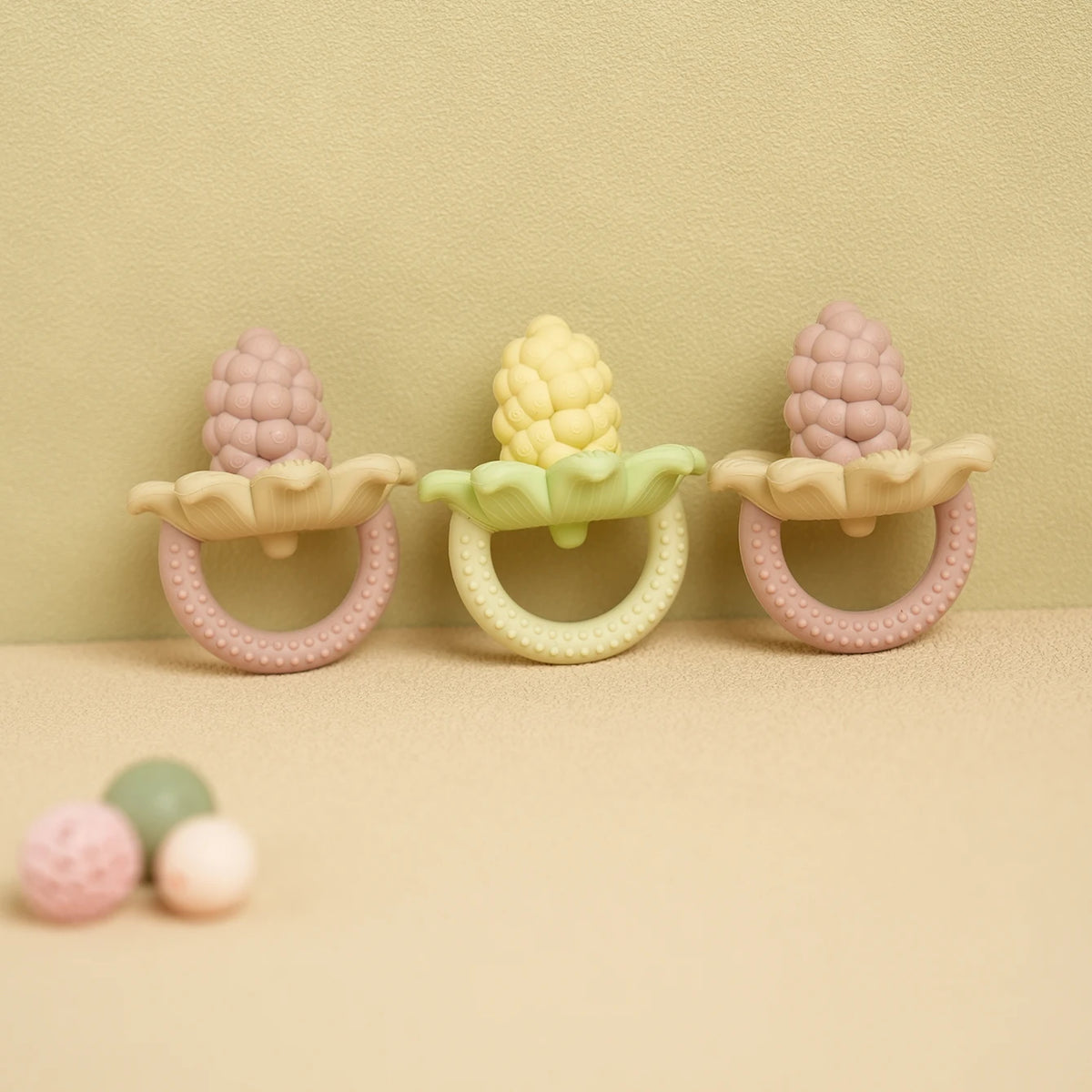Three silicone baby teether toys shaped like flowers and grapes in pink, yellow, and pink.