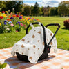 A white stroller cover with gold stars and moons is displayed on an orange checkered mat in a grassy park setting.