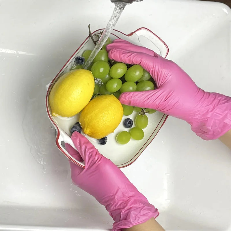 Pink nitrile gloves are washing fresh lemons and green grapes in a white dish.