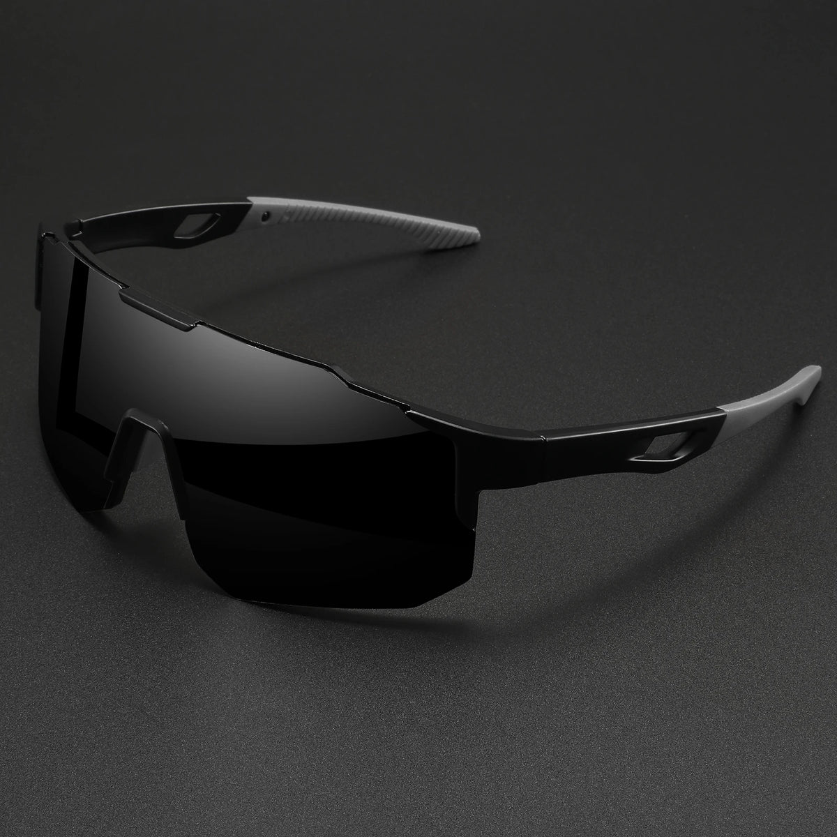 Une paire de lunettes de sport noires oversize à monture enveloppante posées sur une surface sombre.