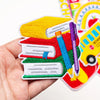 A hand holds a stack of ten colorful back to school iron-on patches featuring books, pencils, and school supplies.