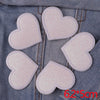 A set of five pink glitter heart iron-on embroidered patches placed on a denim fabric background.