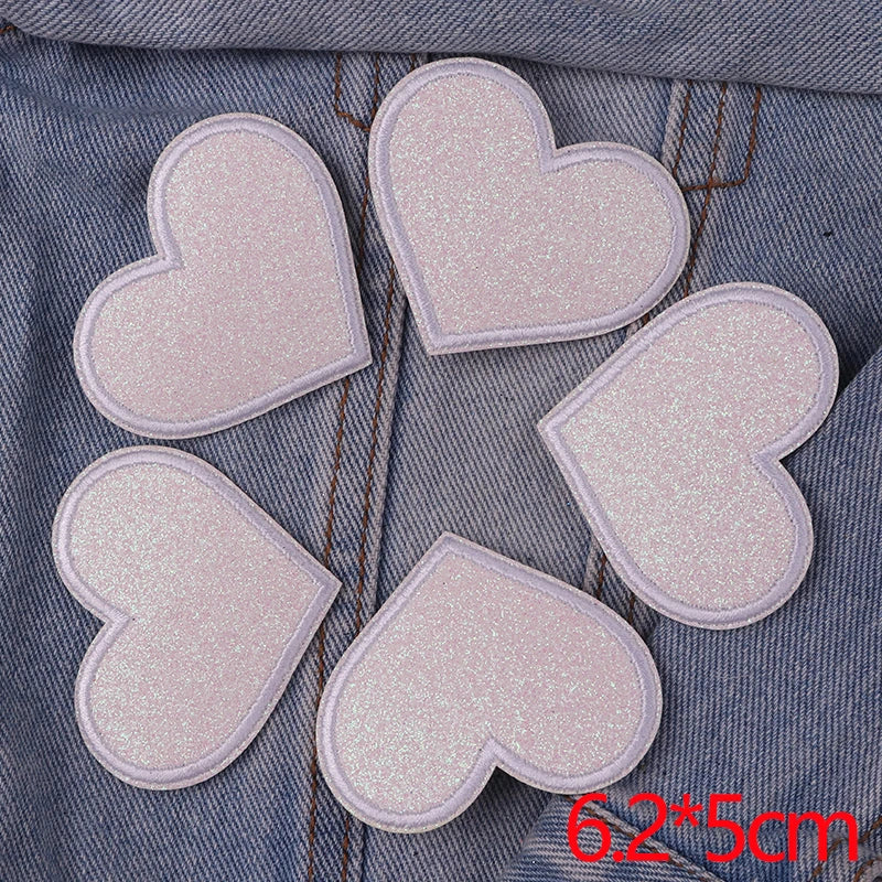 A set of five pink glitter heart iron-on embroidered patches placed on a denim fabric background.