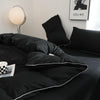 A black duvet cover set with pillows and a silver lamp on a bed.