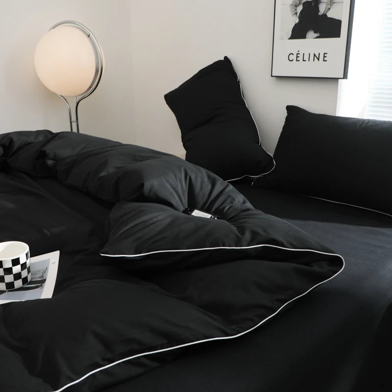 A black duvet cover set with pillows and a silver lamp on a bed.