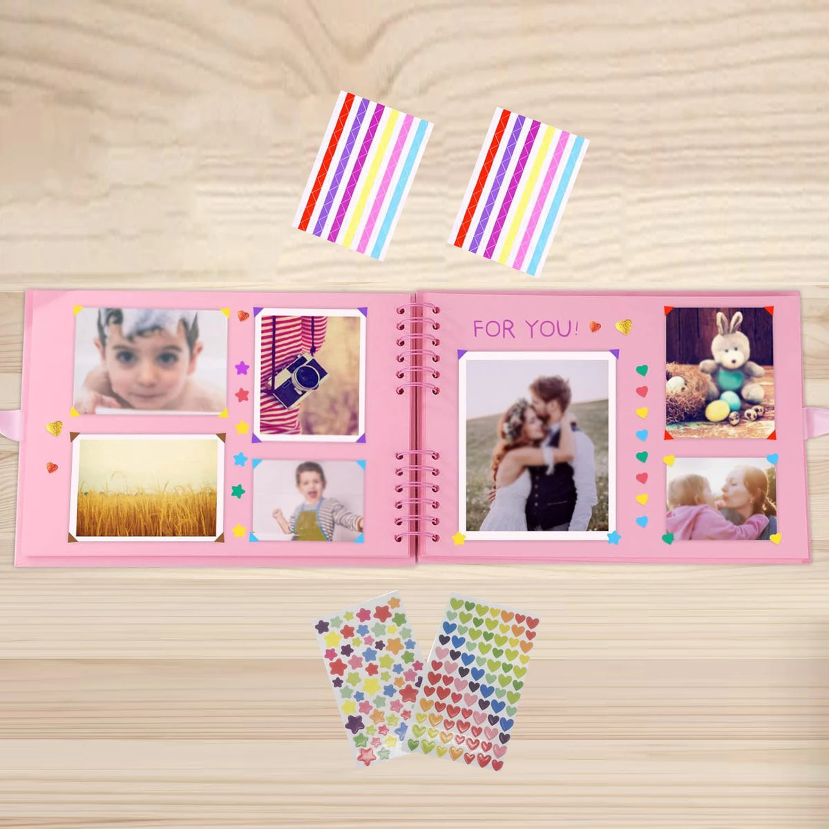 A pink scrapbook album with colorful patterned paper and decorative stickers is shown on a wooden surface.