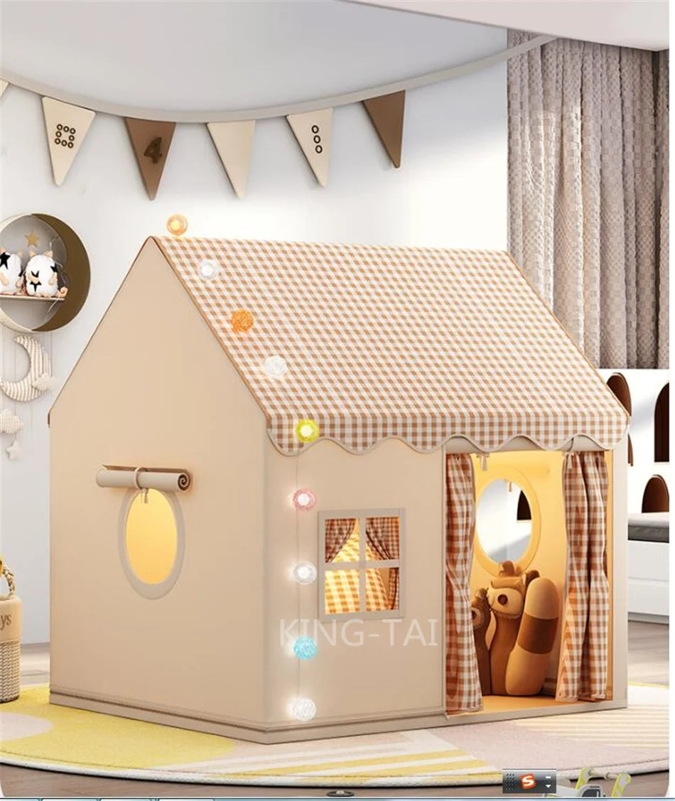 A beige play tent shaped like a house with a straw roof and decorative bunting for children.