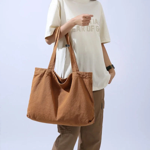 Une femme tient un sac fourre-tout en toile marron et porte un t-shirt blanc et un pantalon beige.