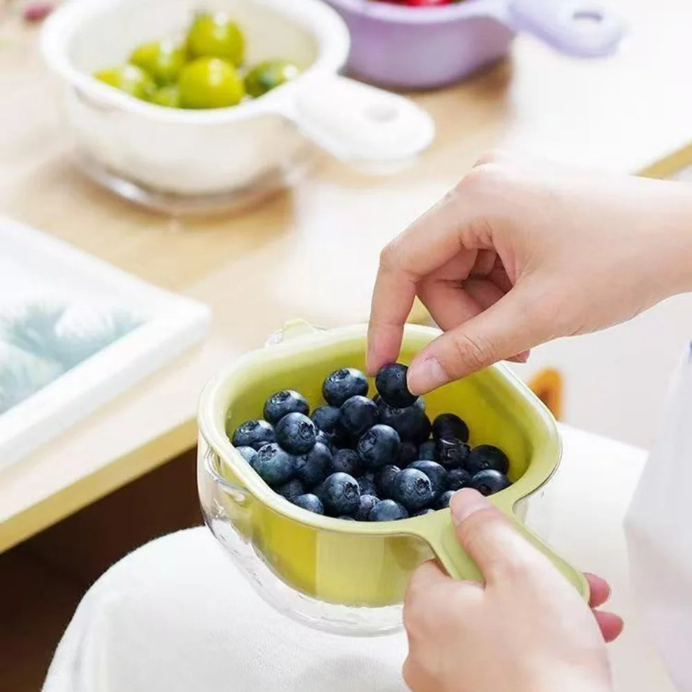 A hand is using a yellow fruit washing basket to hold blueberries for washing or draining.