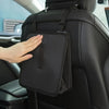 A hand is placing a black foldable car trash can and organizer with a waterproof liner onto the back of a car seat.