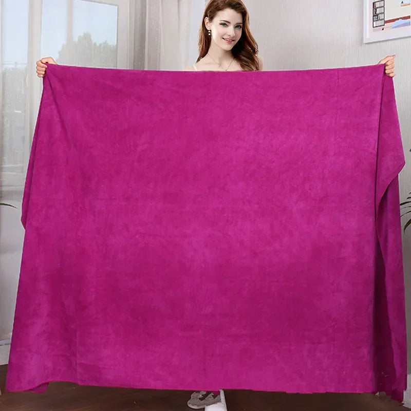 A woman holds up a vibrant magenta microfiber bath towel displaying its texture and color.