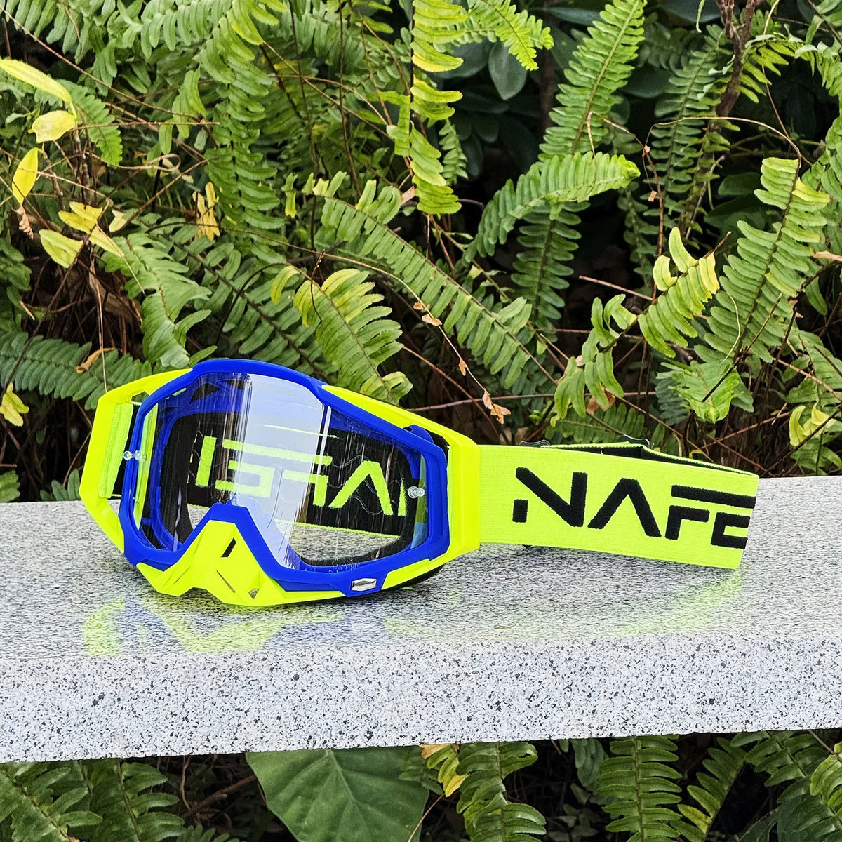 Yellow and blue HD Motocross goggles with anti-fog lens resting on a gray surface.