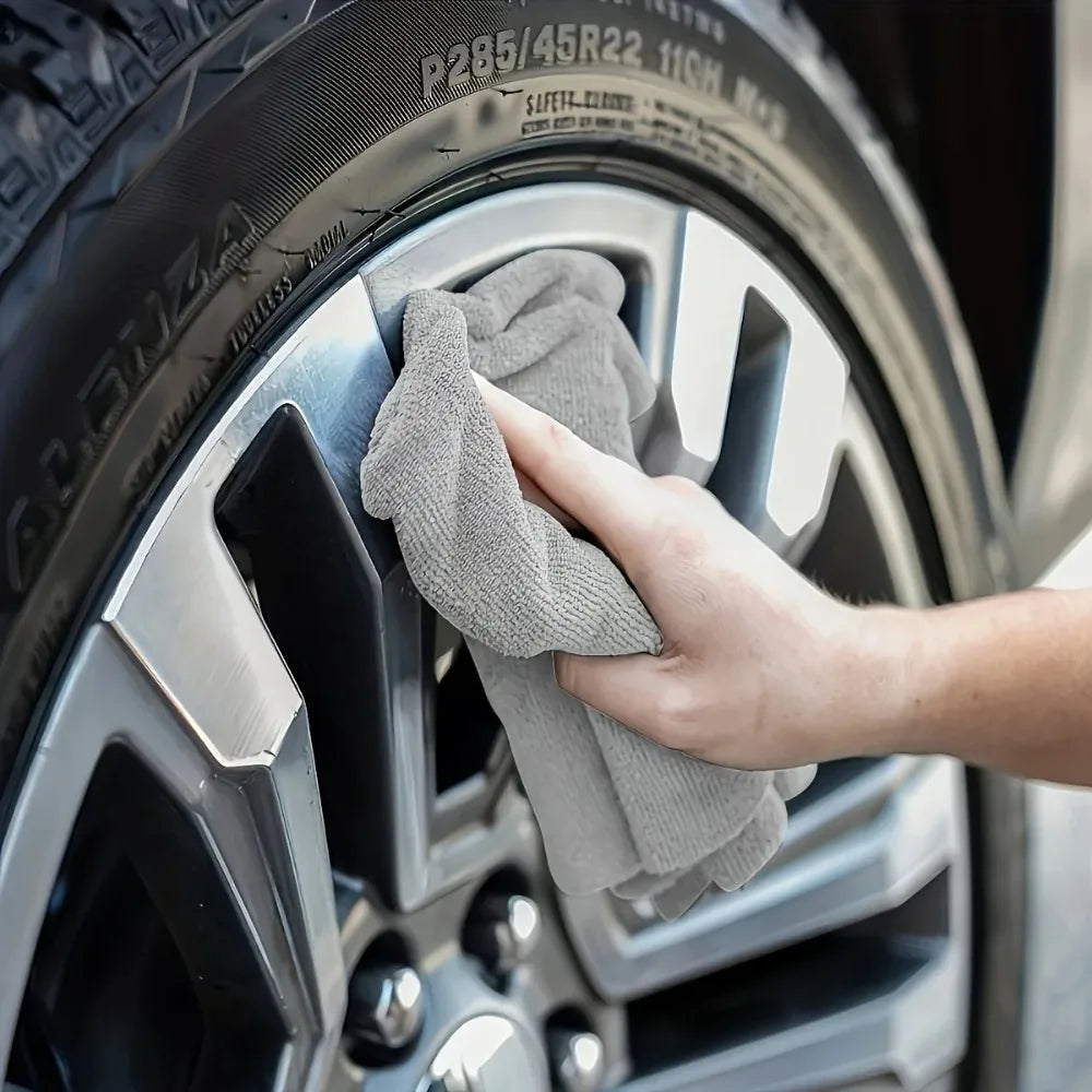 A hand is wiping a gray kitchen cleaning towel set on a car tire rim.