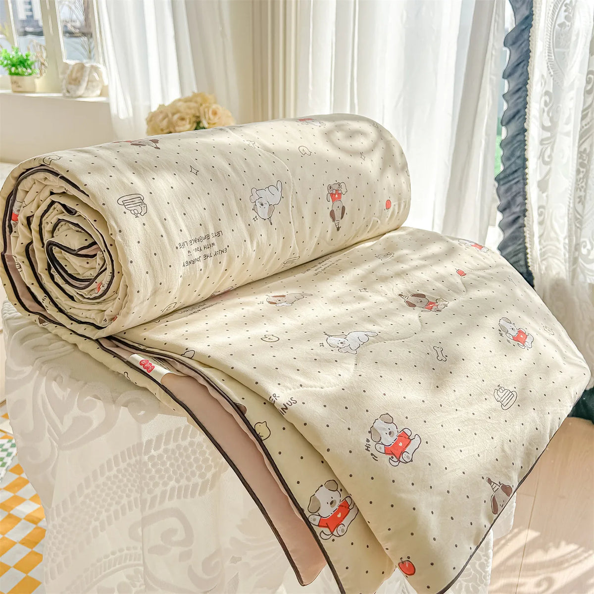 A rolled beige quilt with a pastoral print featuring small animal motifs is displayed on a white surface.