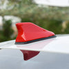 A red aerodynamic shark fin car antenna with a signal amplifier mounted on a silver car roof.