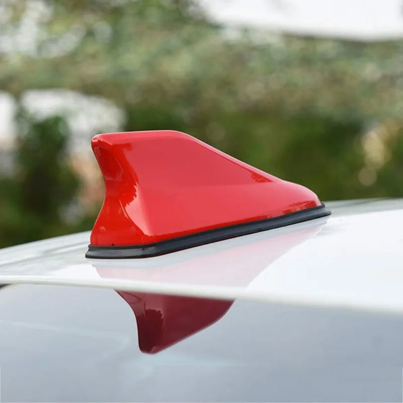 A red aerodynamic shark fin car antenna with a signal amplifier mounted on a silver car roof.