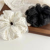 A pair of black polka dot mesh scrunchie hair ties resting on a light fabric next to white polka dot ones.