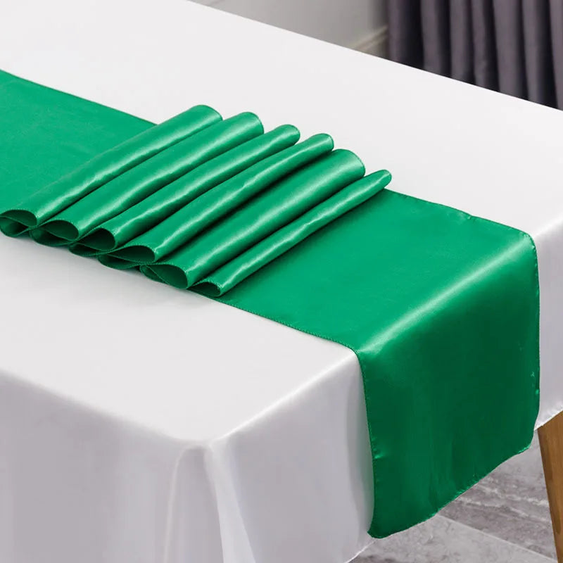 A vibrant green satin table runner is neatly folded on a white tablecloth for an elegant event setting.