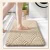 A beige plush velvet bathroom mat with a diamond pattern is placed on a white floor.