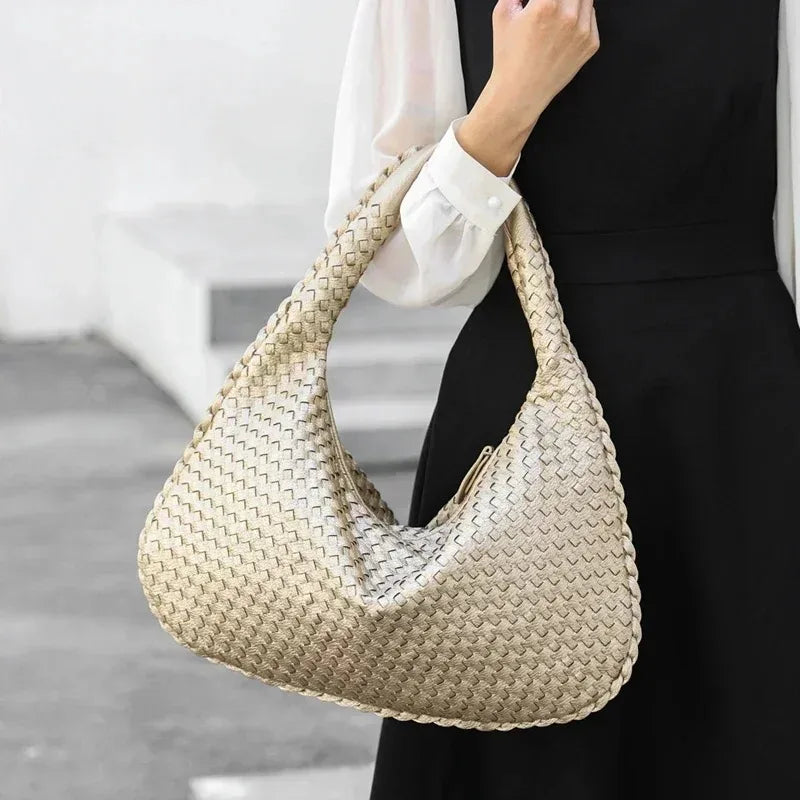 A beige woven vegan leather hobo bag being held by a person against a dark background.
