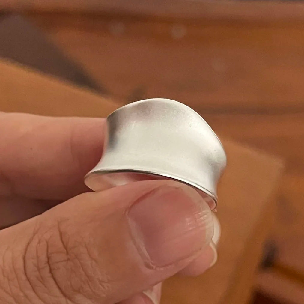 A close-up of a minimalist sterling silver ring with a curved design being held by a hand.
