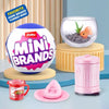 A collection of Mini Brands toys, including a spherical toy, a glass bowl with an orange toy, and a pink microwave-like item.