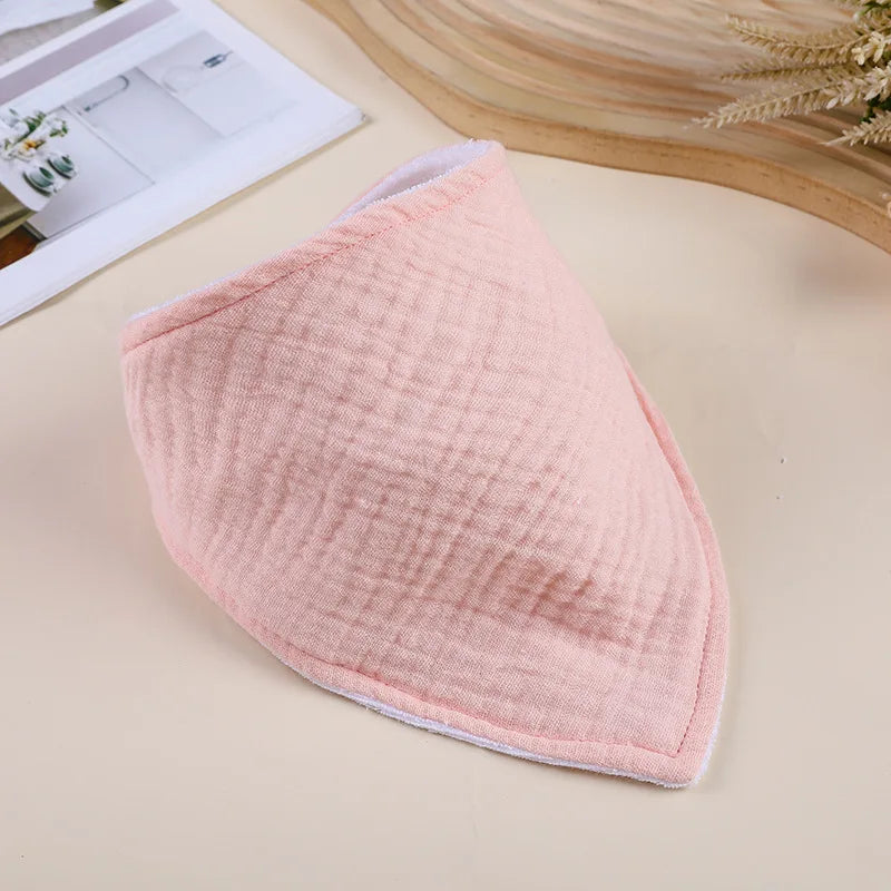 A soft pink cotton baby bib with a textured surface is shown on a light background.