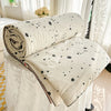 A cream-colored quilt with black polka dots is rolled up and displayed on a white surface.