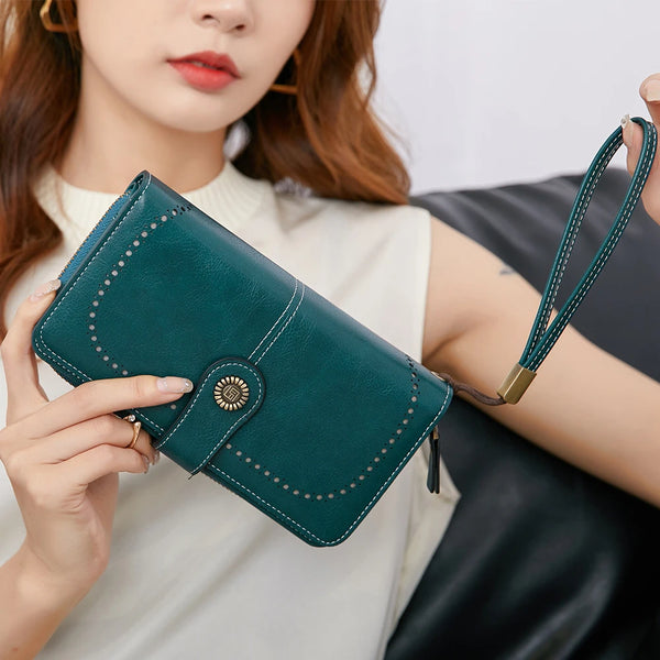 A close-up of a dark teal vintage RFID-blocking wallet with a gold accent and leather wrist strap being held by a woman.
