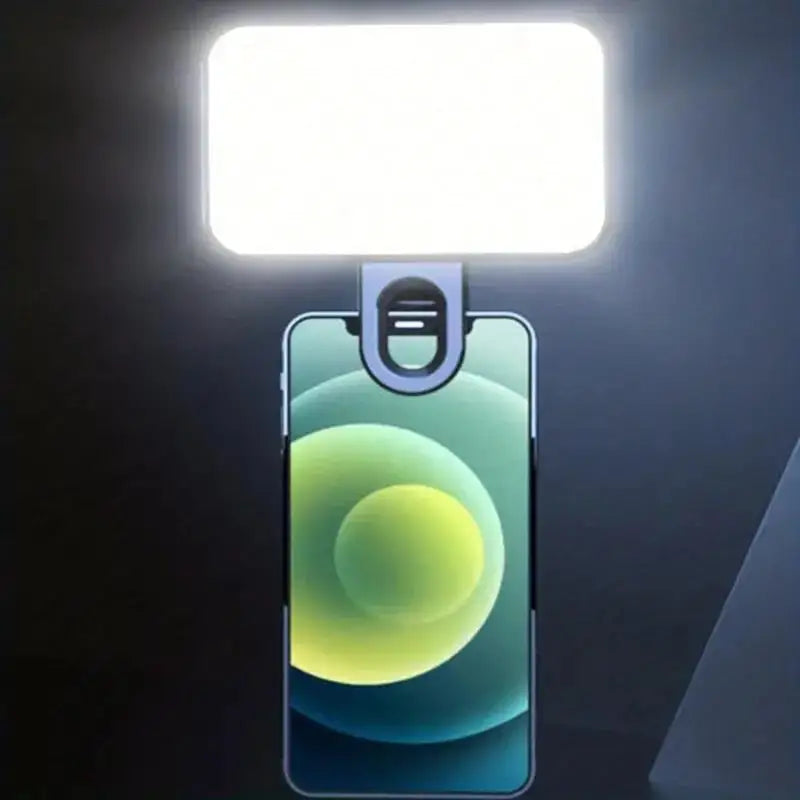 A smartphone is illuminated by a bright, rectangular LED light clip-on accessory.