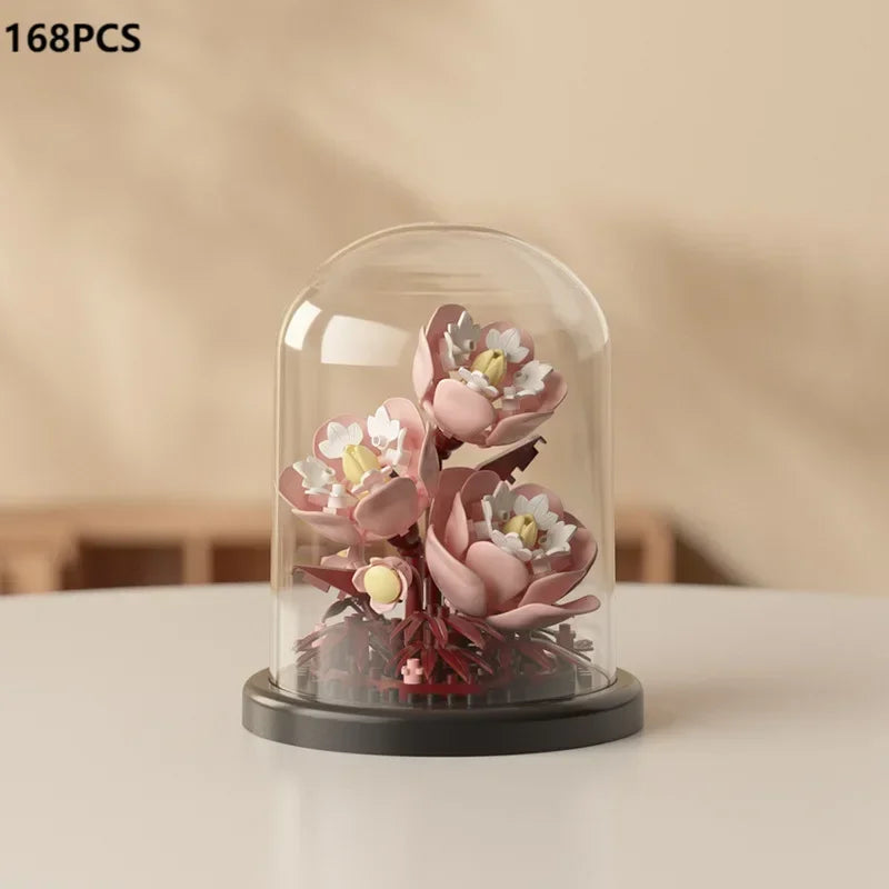A clear glass cloche displays a small arrangement of pink and white artificial roses and greenery.
