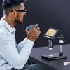 A man is using a digital microscope to examine a small object on a dark surface.