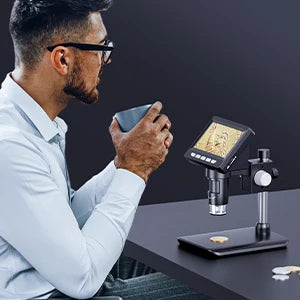 A man is using a digital microscope to examine a small object on a dark surface.