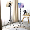 A black adjustable aluminum tripod stand is shown next to a tablet, set up in a bright indoor environment.