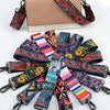 A beige crossbody bag with a patterned strap featuring geometric designs in red, orange, and blue.