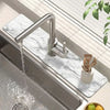A modern stainless steel faucet is shown pouring water onto a marble drying mat placed over a kitchen sink.