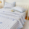 Light blue and white striped quilted bedspread with small floral embroidery on a bed.