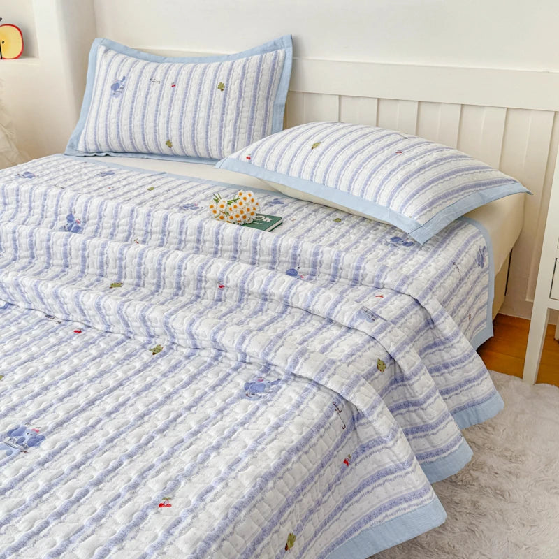 Light blue and white striped quilted bedspread with small floral embroidery on a bed.