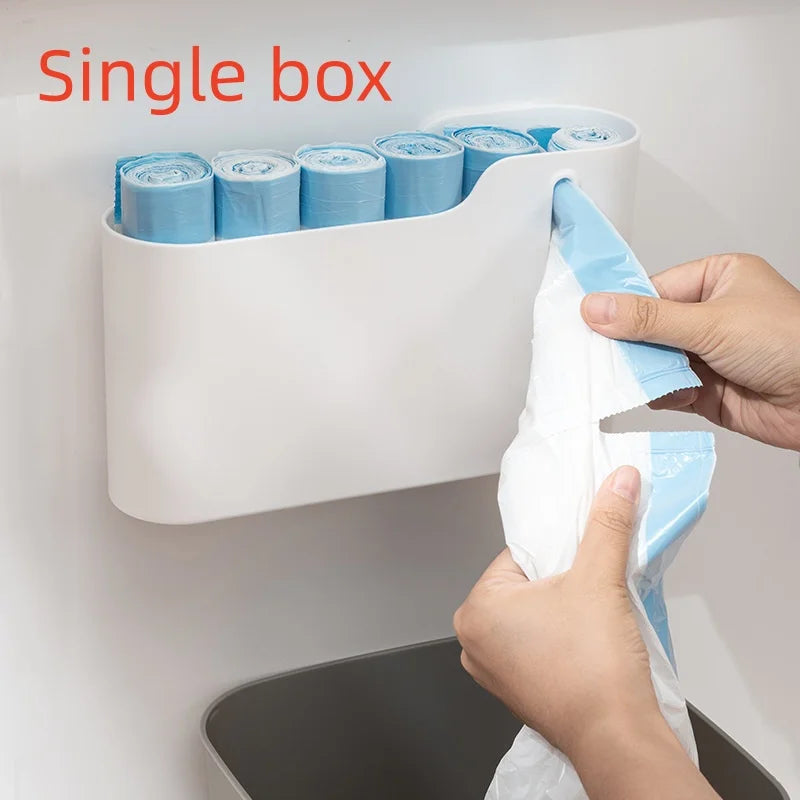 A white single box dispenser for scented drawstring trash bags with handles is mounted on a wall.