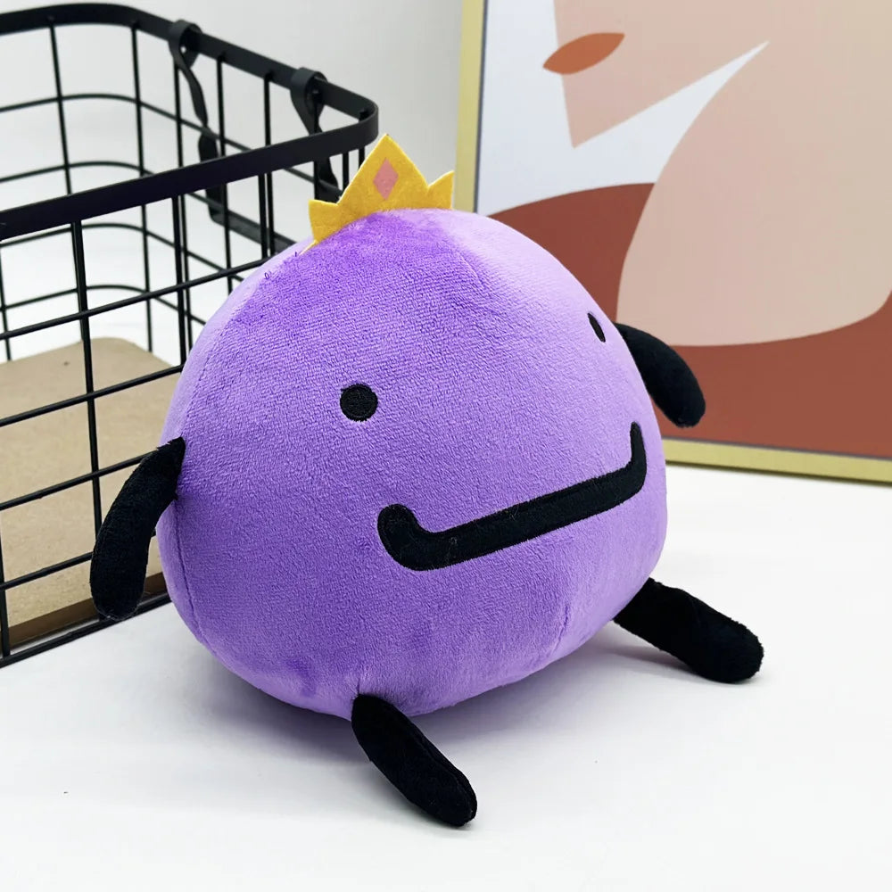 A cute purple plush doll with a gold crown and black features sitting on a white surface.