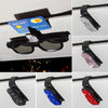 Black sunglasses clip with crystal rhinestones and colored accents mounted on a car visor.