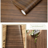 Roll of brown sandalwood wood grain wallpaper showing texture and application on a wooden surface.
