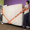 A man is using orange furniture moving straps with shoulder pads to secure a large, quilted white piece of furniture.